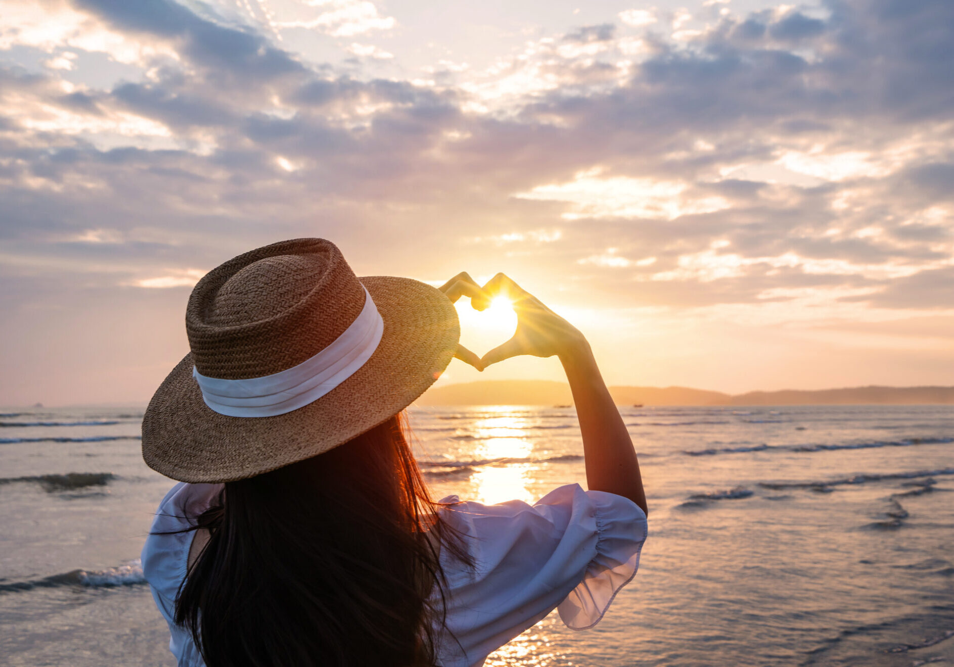 Dame formt Herz aus Fingern bei Sonnenutnergang